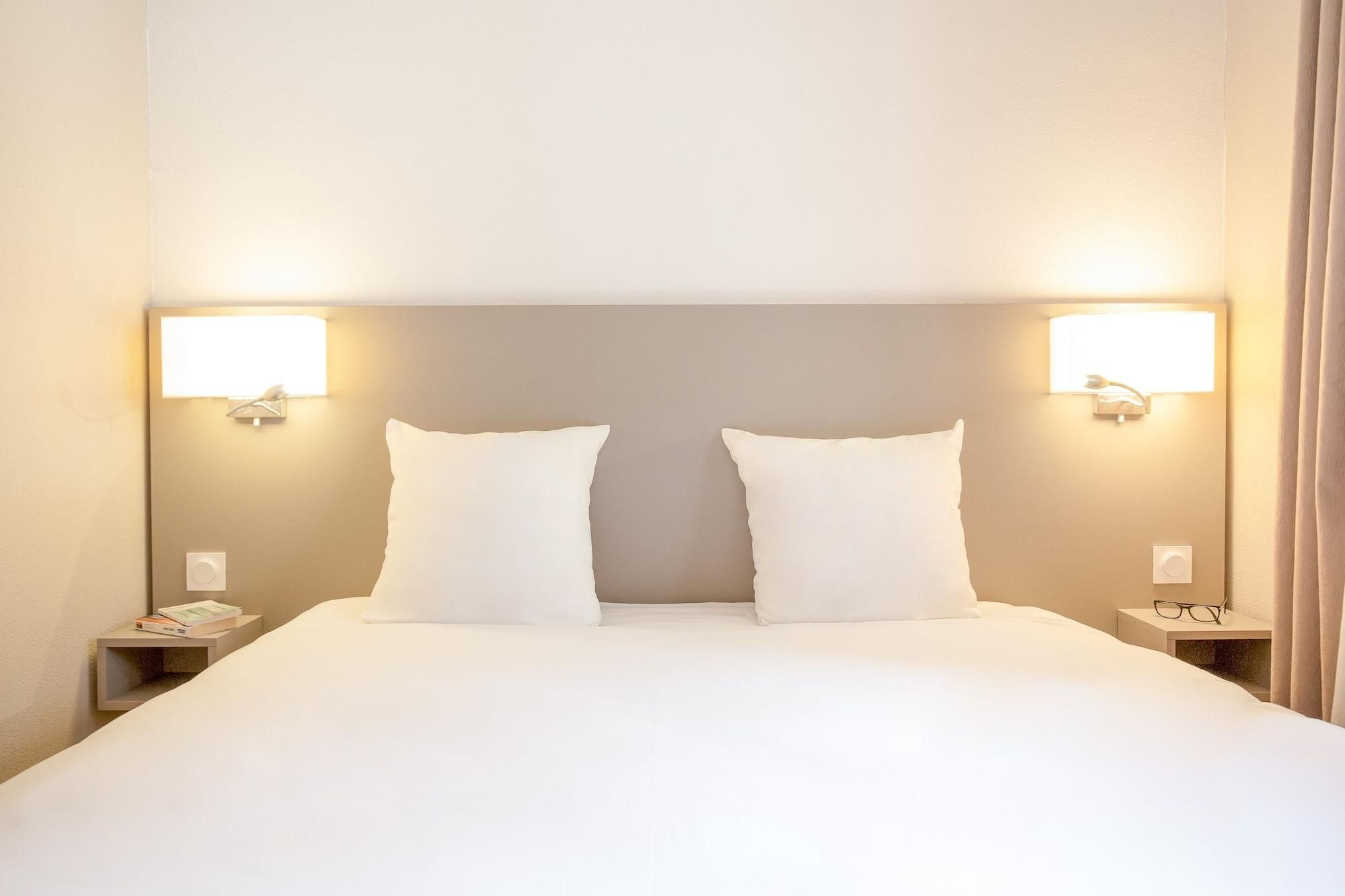 A hotel room with a large bed, two bedside tables, and wall-mounted lamps.