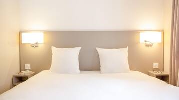 A hotel room with a large bed, two bedside tables, and wall-mounted lamps.