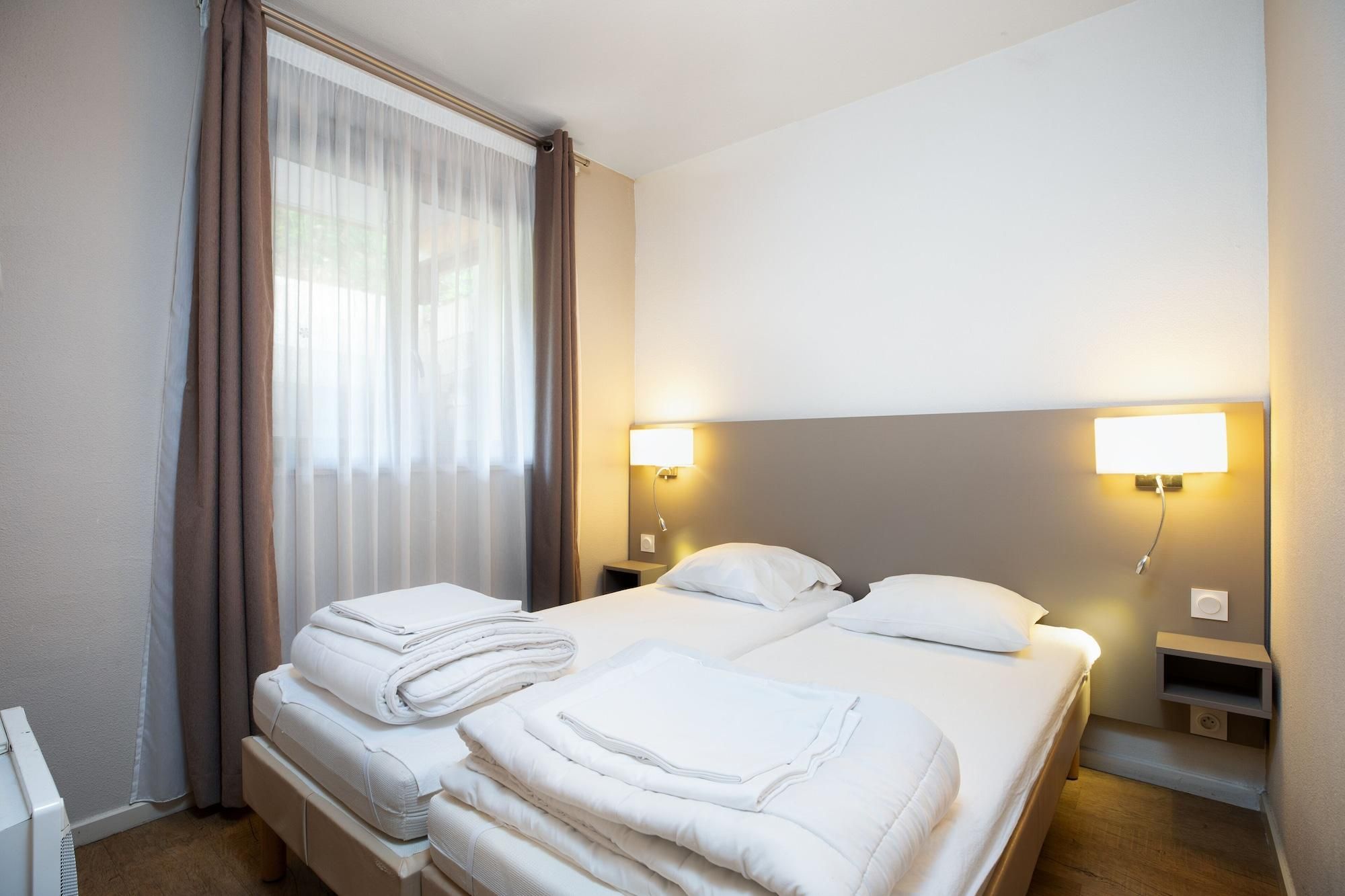 Een hotelkamer met een bed, twee nachtkastjes, een lamp en een raam met gordijnen.