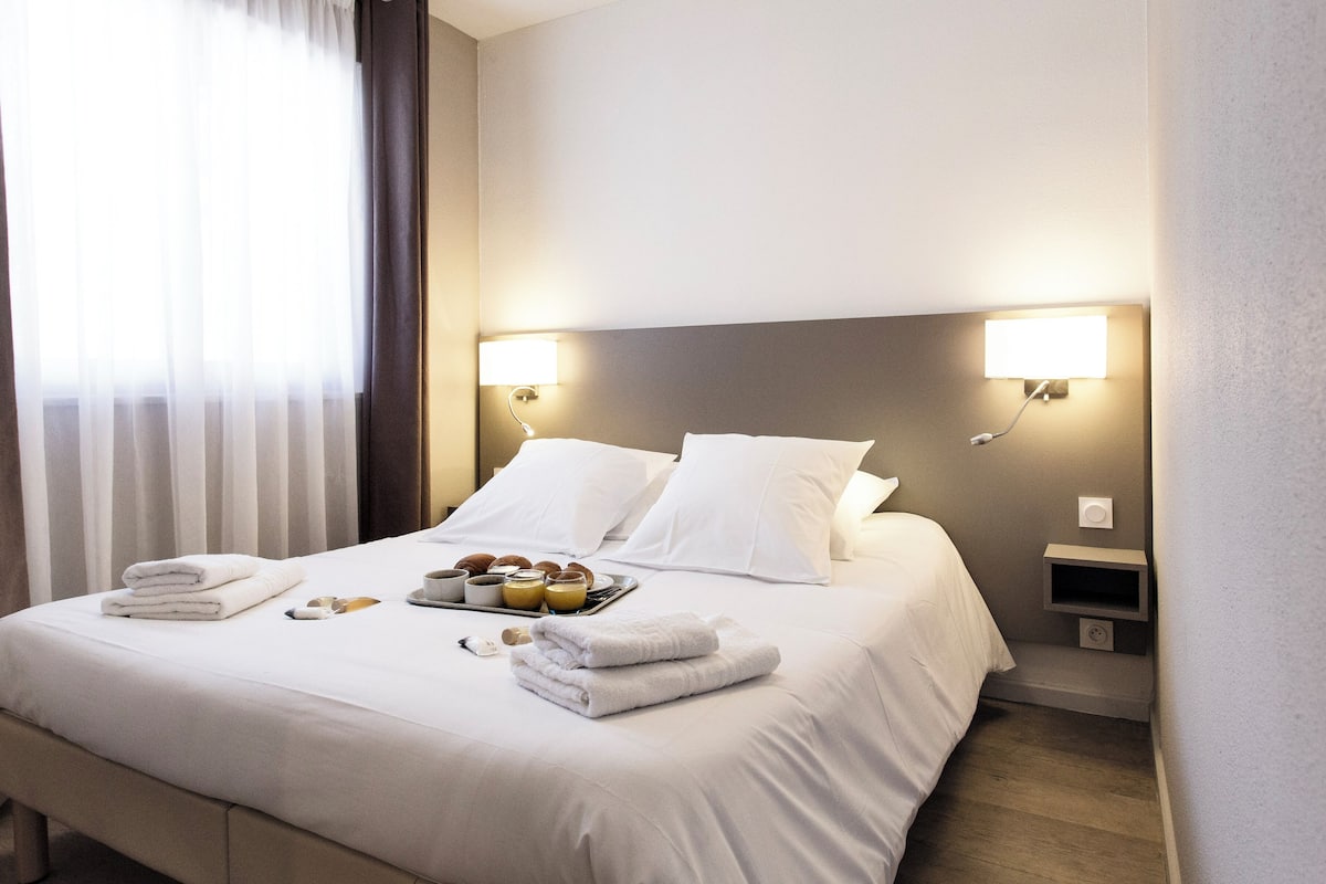 A neatly made bed with white linens, two bedside lamps, and a tray of breakfast items.