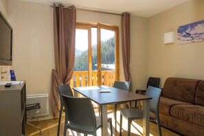 A room with a table and chairs, a sofa, a window with curtains, a radiator, and a television on the wall. - Sowell Residences Pra Loup (Uvernet-Fours)