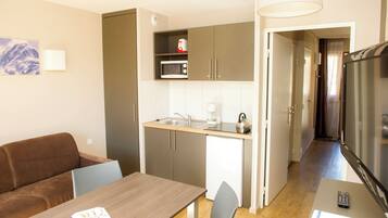 A compact kitchen with a microwave, coffee maker, and kettle, a dining area with a table and chairs, and a living area with a sofa and a TV.