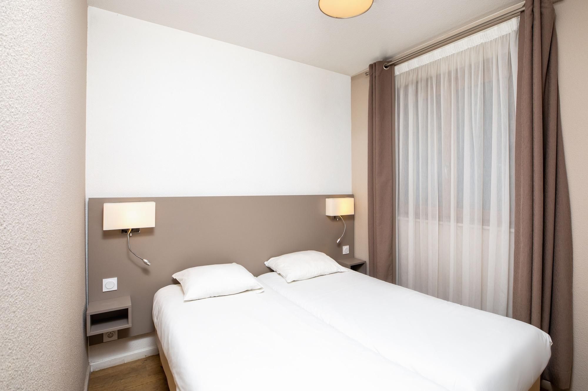 Una habitación de hotel con una cama individual, dos mesitas de noche y un ventanal con cortinas.