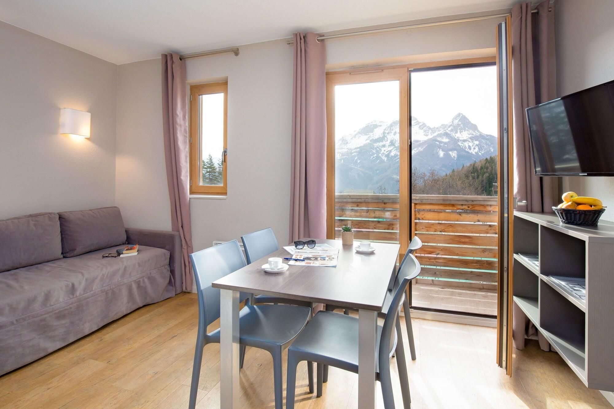 Una habitación moderna con sofá, mesa de comedor, sillas, televisión y vistas a las montañas.