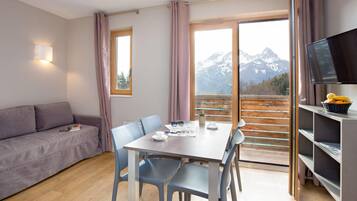 Una habitación moderna con sofá, mesa de comedor, sillas, televisión y vistas a las montañas.