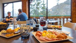 A dining table with various dishes, a glass of red wine, and a view of a mountain through large windows. - Sowell Residences Pra Loup (Uvernet-Fours)