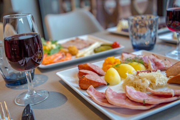 A dining table with plates of food, a glass of red wine, and a glass of water. - Sowell Residences Pra Loup (Uvernet-Fours)