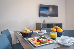 A breakfast setup with croissants, fruit, and a plate of assorted meats and cheeses on a table with a TV in the background. - Sowell Residences Pra Loup (Uvernet-Fours)