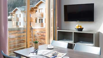 Una habitación con una mesa de comedor, sillas, televisor y ventana con vistas a edificios y montañas.