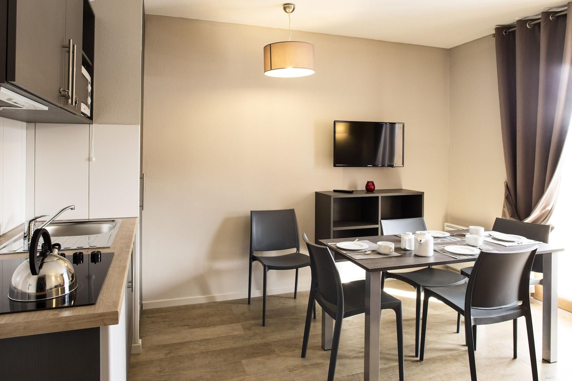 Una cocina moderna con estufa integrada, un comedor con mesa lista para dos personas y un televisor de pantalla plana montado en la pared.