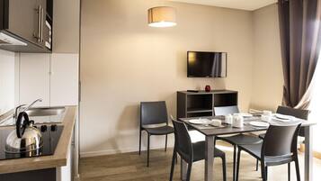 Una cocina moderna con estufa integrada, un comedor con mesa lista para dos personas y un televisor de pantalla plana montado en la pared.