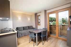 A compact living space with a kitchenette, a sofa, a dining table with chairs, and a sliding glass door leading to a balcony. - Sowell Residences Pra Loup (Uvernet-Fours)