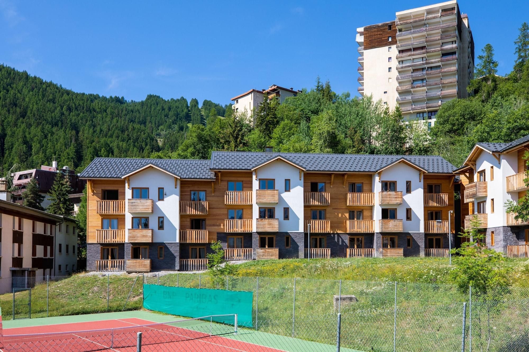 Una hilera de edificios de madera de varios pisos con balcones, frente a un paisaje de colinas boscosas.