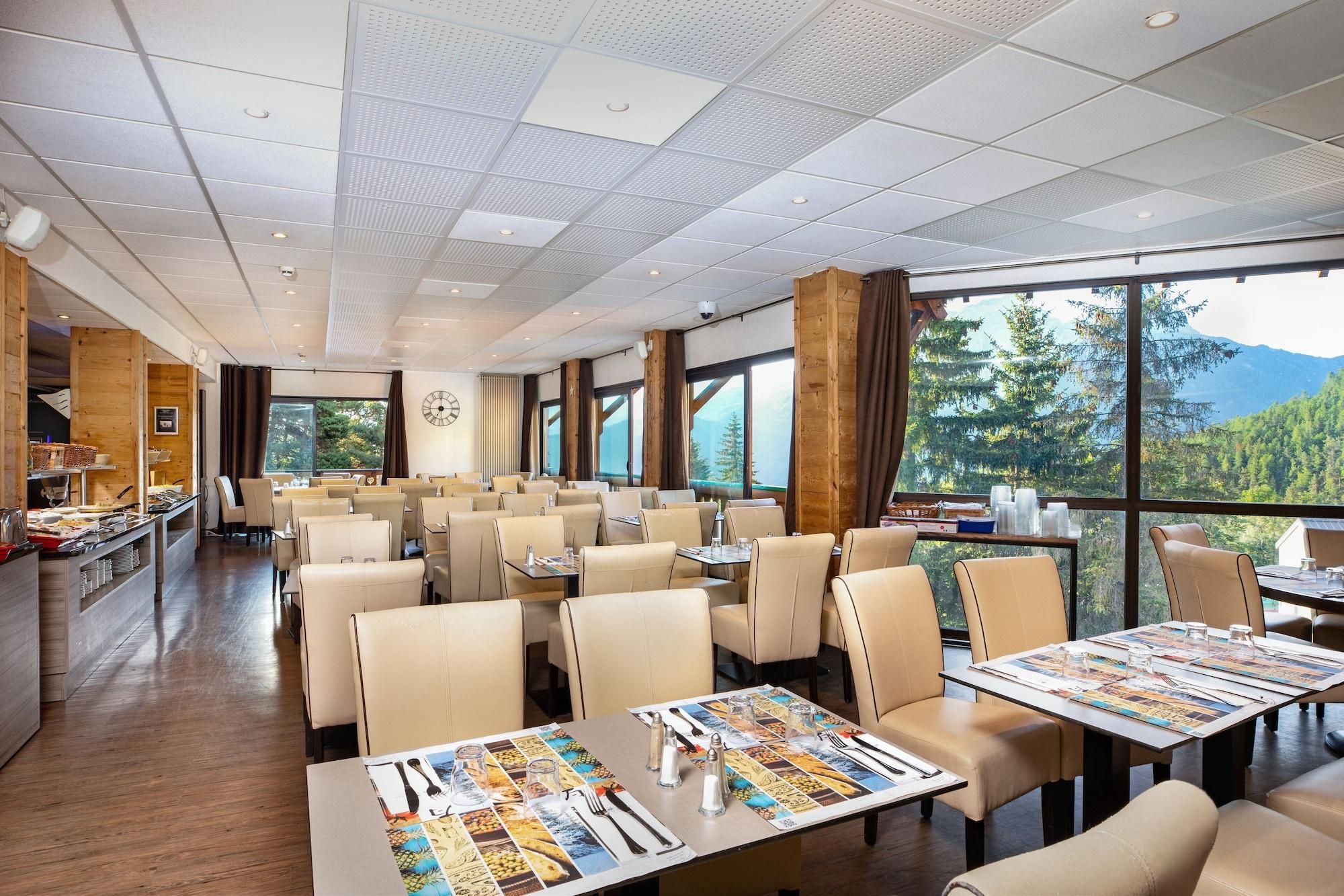 Un vaste espace dédié à la salle à manger, avec de grandes tables et des chaises hautes, de grandes fenêtres offrant une vue sur les montagnes et un buffet situé sur le côté gauche.