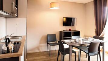 A modern kitchen with a kettle, a dining table set for four, and a TV mounted on the wall.