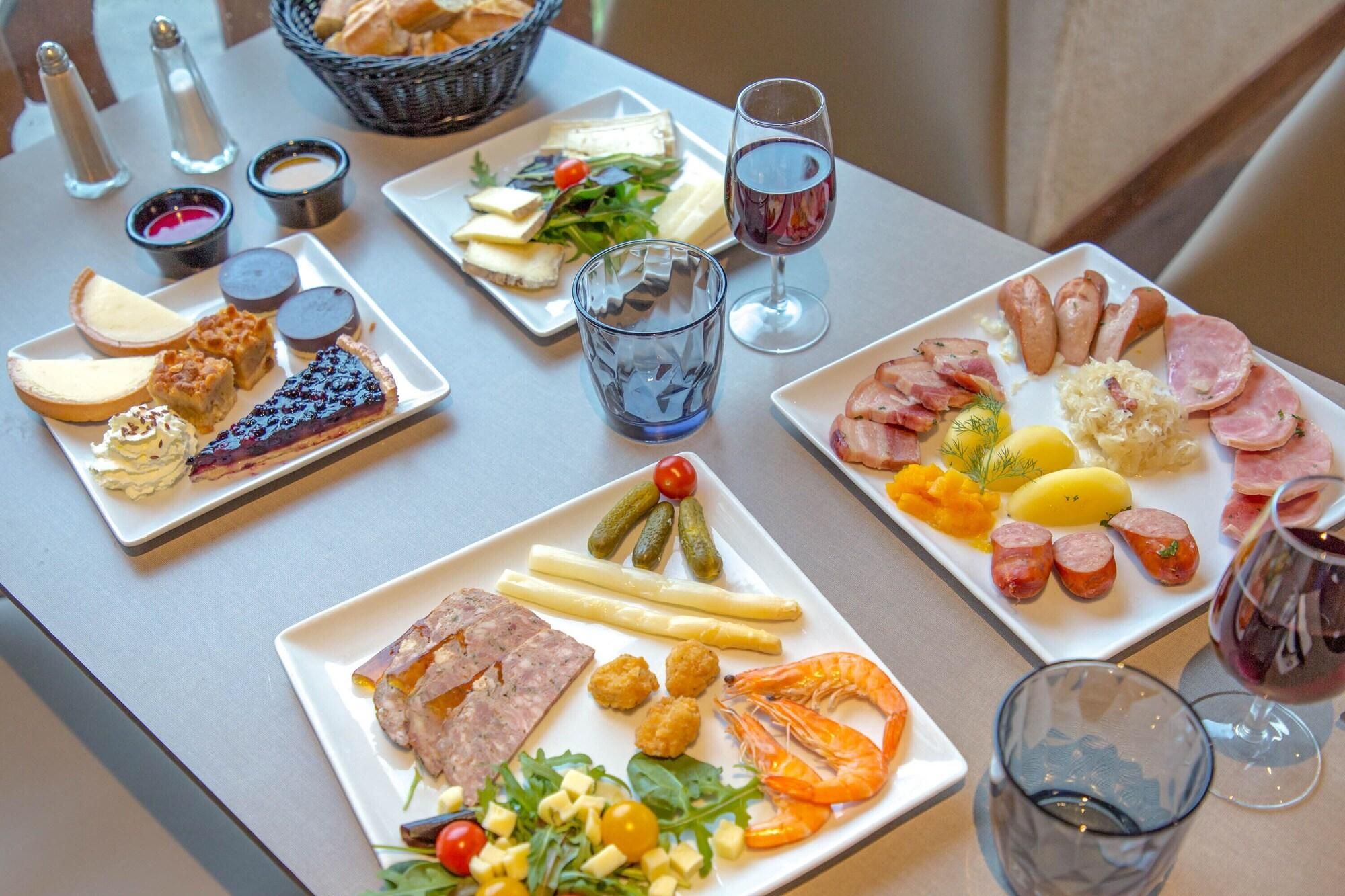 Una mesa servida con diversos platos, incluyendo carnes, quesos y una tarta, junto con copas de vino tinto.