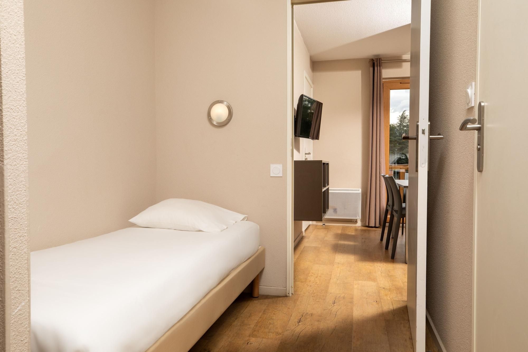 Una habitación pequeña con cama individual, suelo de madera, una mesita de noche y televisor montado en la pared.