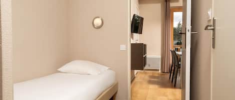 A small, single-bed room with a wooden floor, a bedside table, and a wall-mounted TV.
