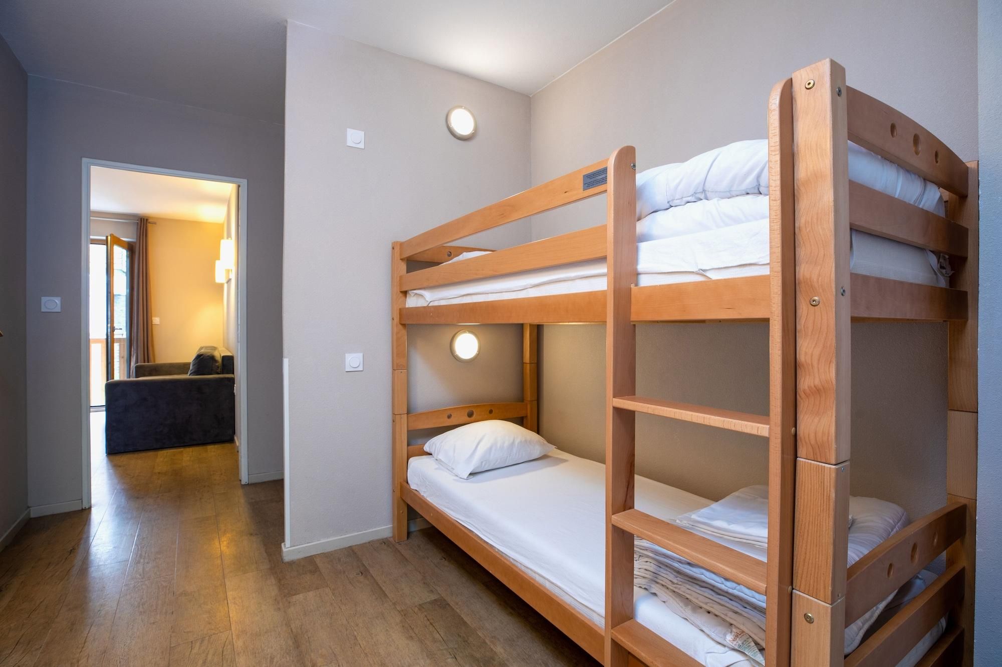 A bunk bed room with a wooden floor and a small seating area with a chair and a table.