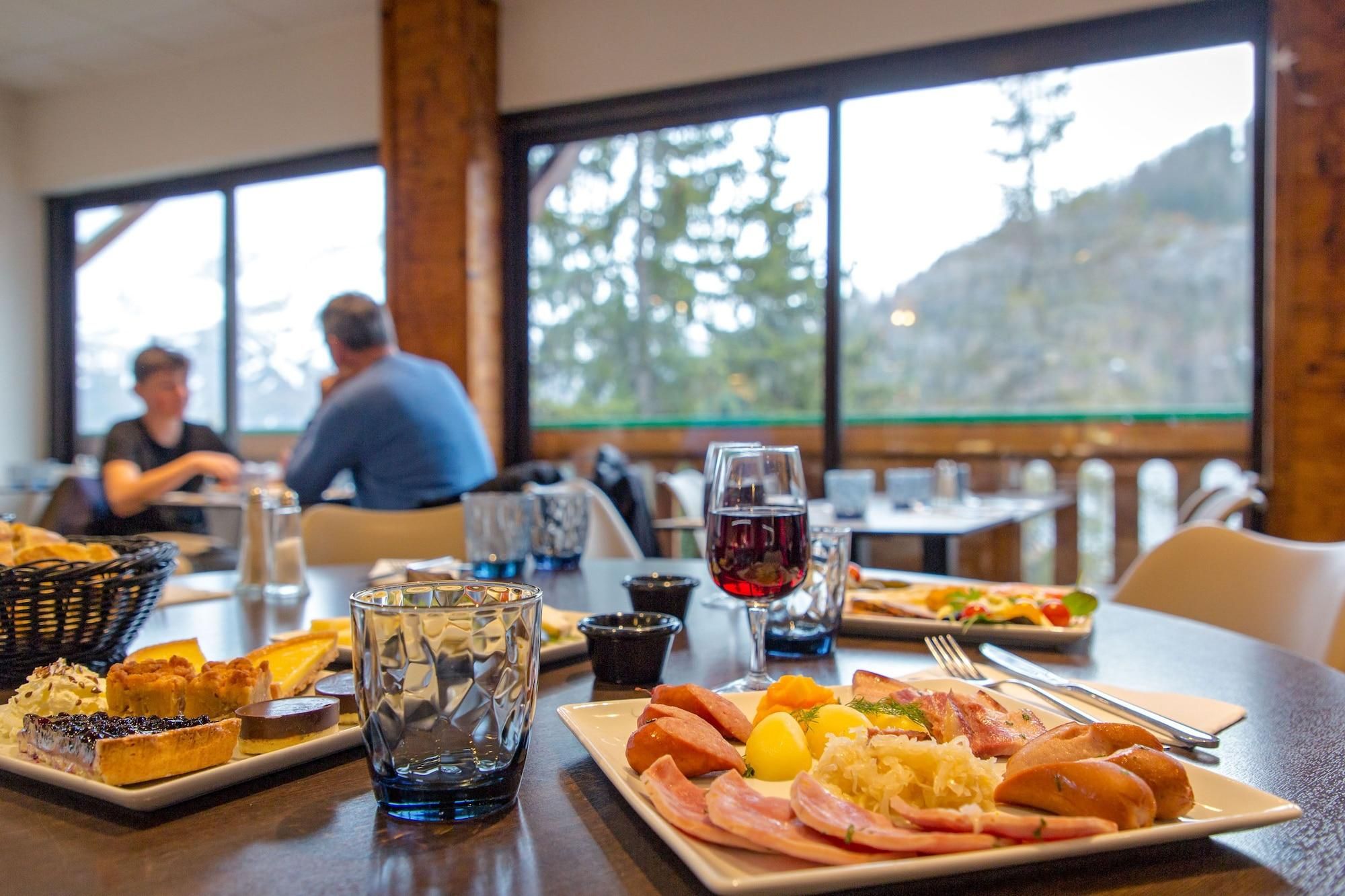 Una mesa de comedor con diversos platos, una copa de vino tinto y vistas a la montaña a través de amplios ventanales.