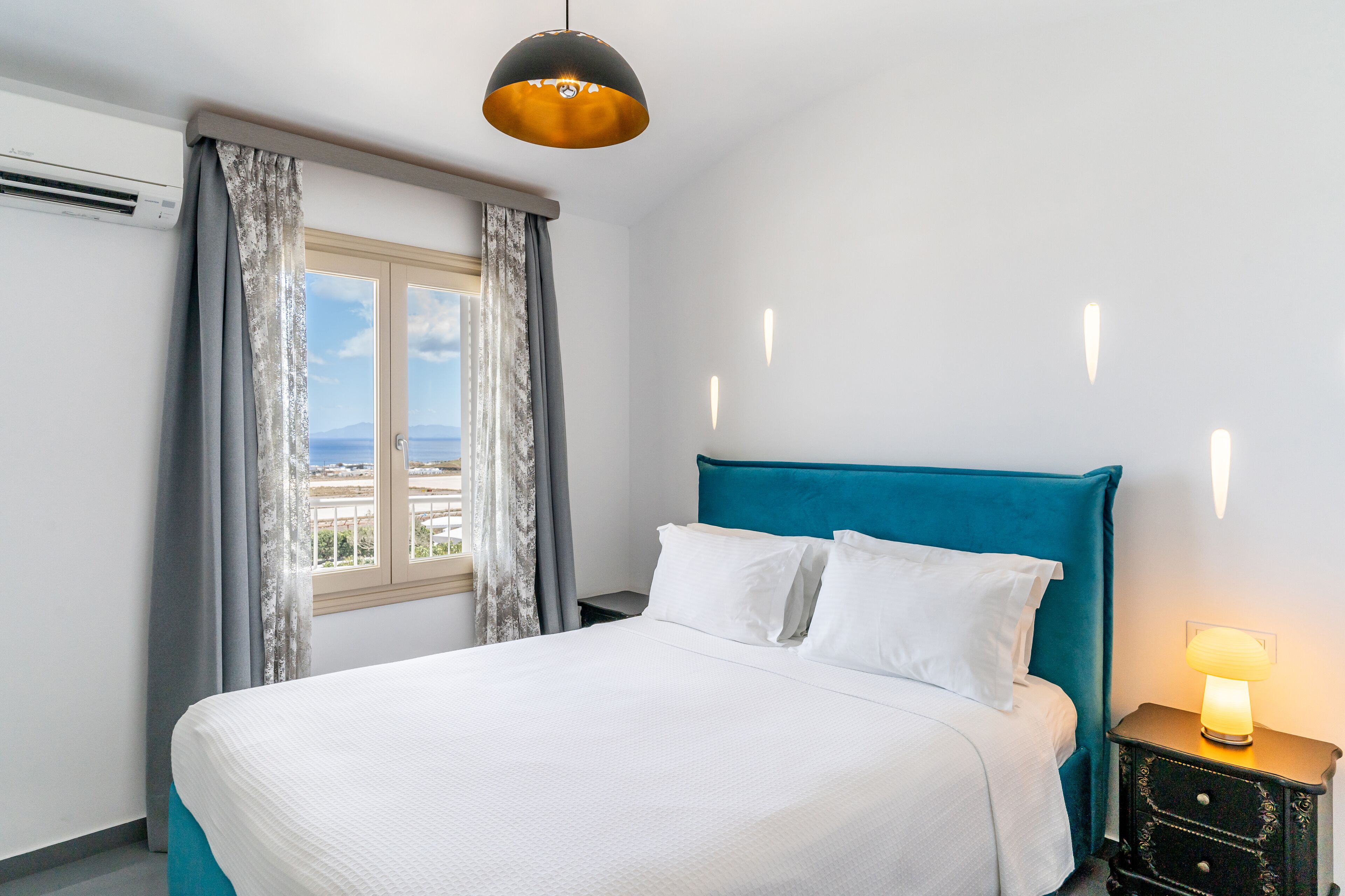 A hotel room with a bed, a nightstand with a lamp, a window with curtains, and a view of the city.