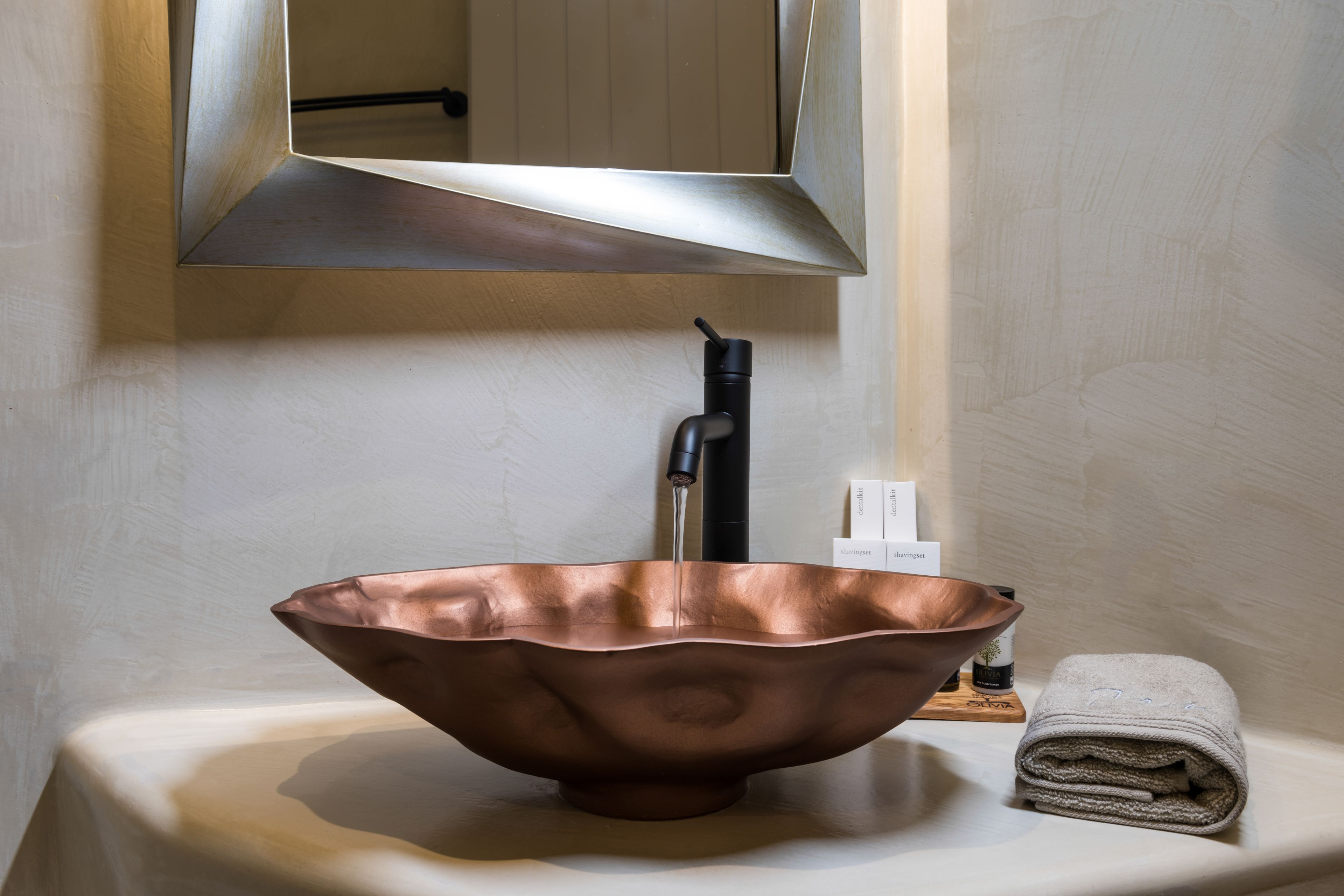 Un lavabo de cobre sobre una encimera blanca con un grifo negro, un espejo arriba y una toalla doblada a la derecha.