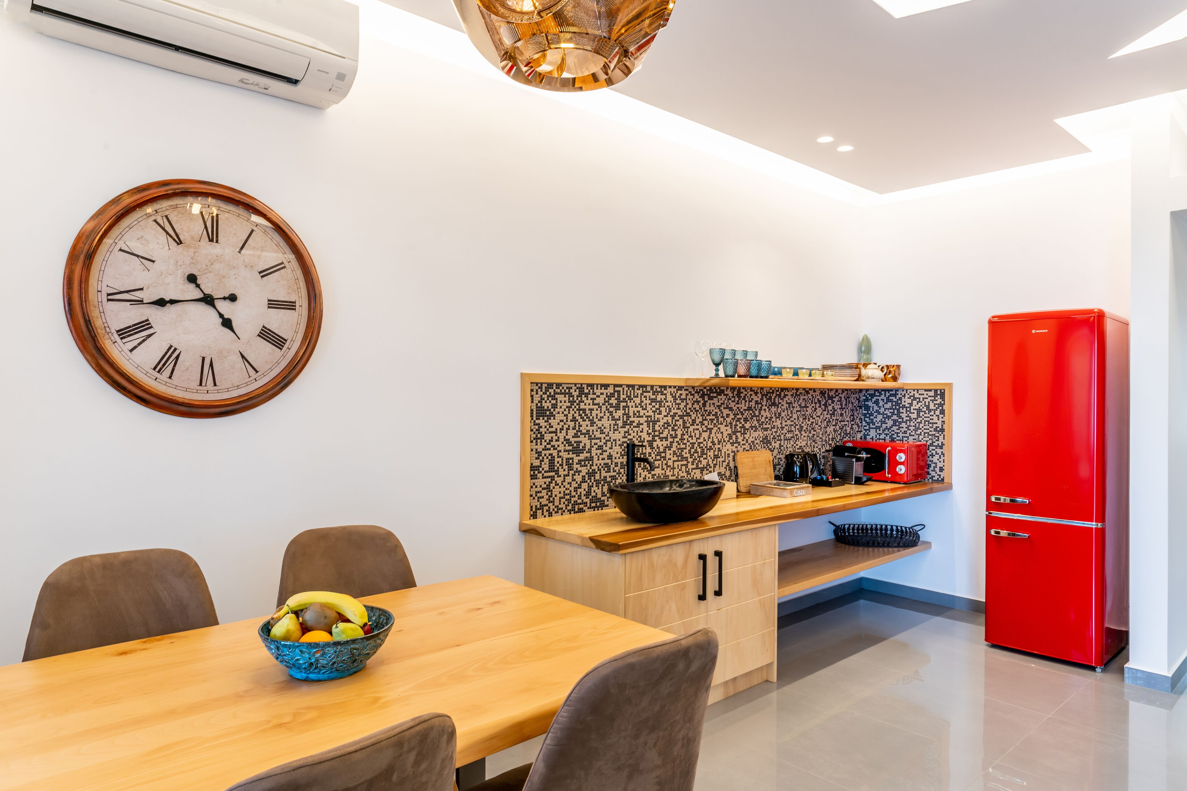 A modern kitchen with a wooden dining table, a red refrigerator, and a mosaic backsplash.