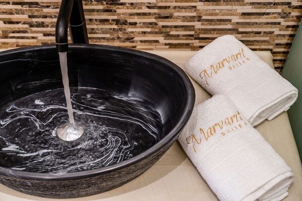 Un lavabo negro con agua corriendo, dos toallas blancas con el bordado 'Marriott Suites' y una pared de azulejos al fondo.