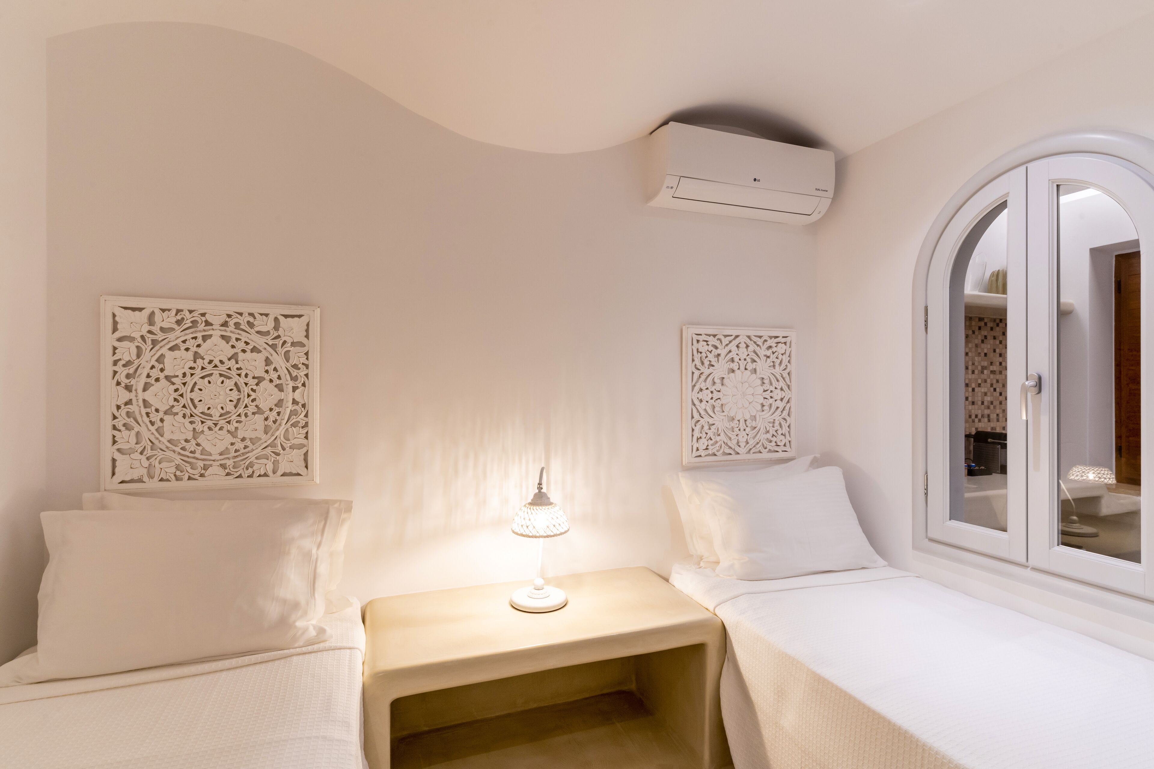 Un dormitorio con dos camas, una mesita de noche con lámpara, paneles decorativos en la pared, un equipo de aire acondicionado y una ventana con vistas al exterior.