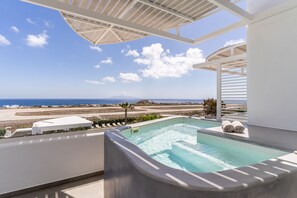 Un área de piscina con vistas a la playa y al océano, una pérgola blanca y sillones de descanso.