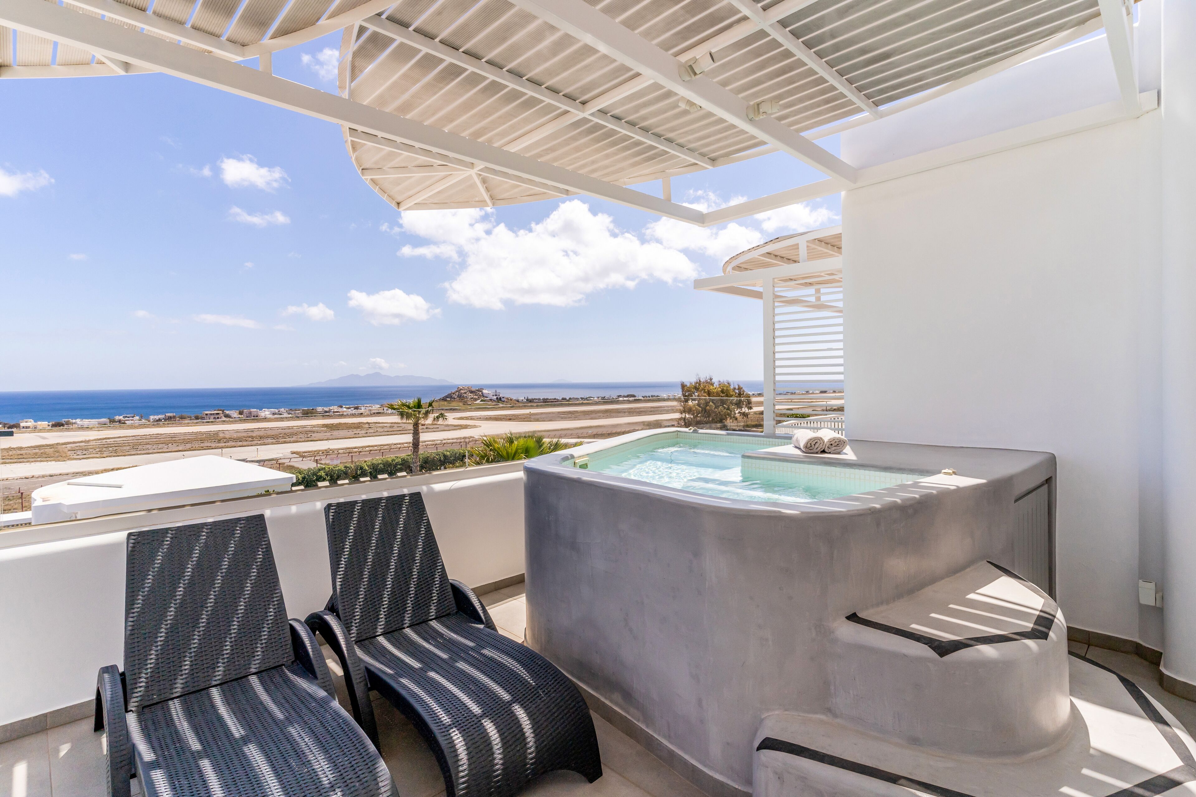 Un balcón con dos sillones de mimbre, una bañera de hidromasaje y vistas al mar y la playa.
