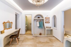 A hallway with a vanity, a mirror, a chair, a shoe rack, and a door leading to a bathroom.