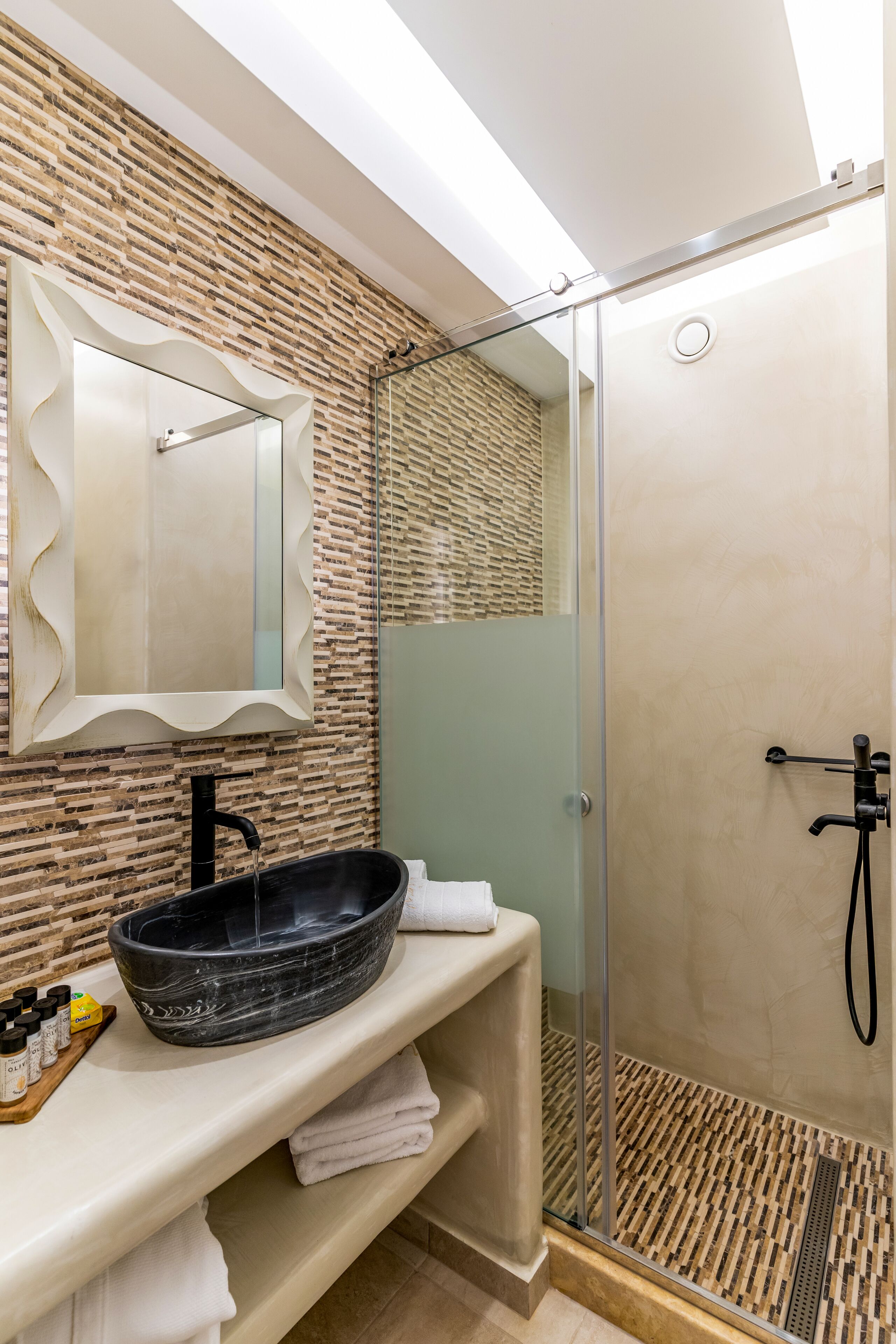 Un baño moderno con un lavabo de estilo pedestal negro, una ducha con cerramiento de vidrio y un espejo con un marco original.