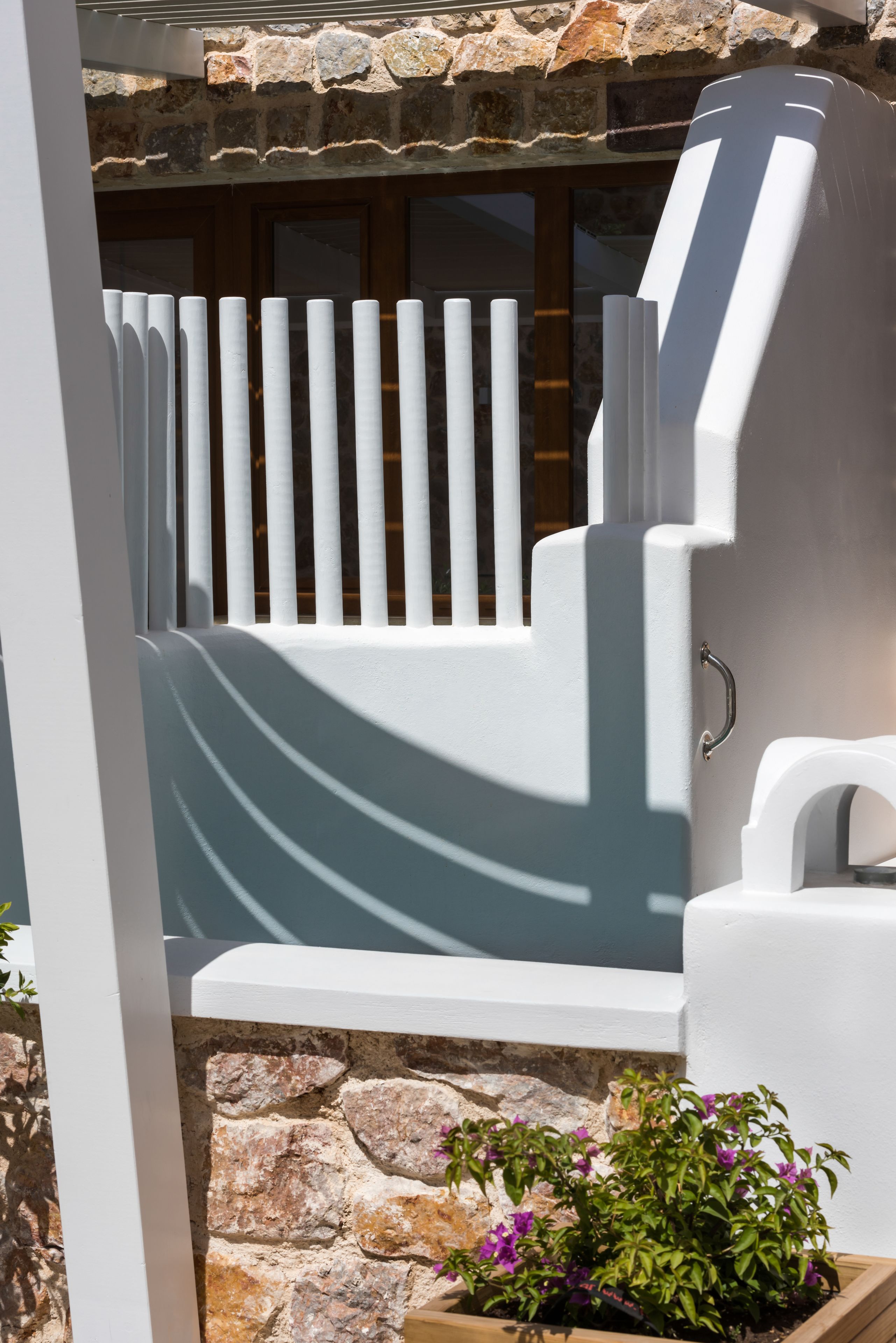 A modern outdoor seating area with a stone wall backdrop, white railings, and a potted plant.