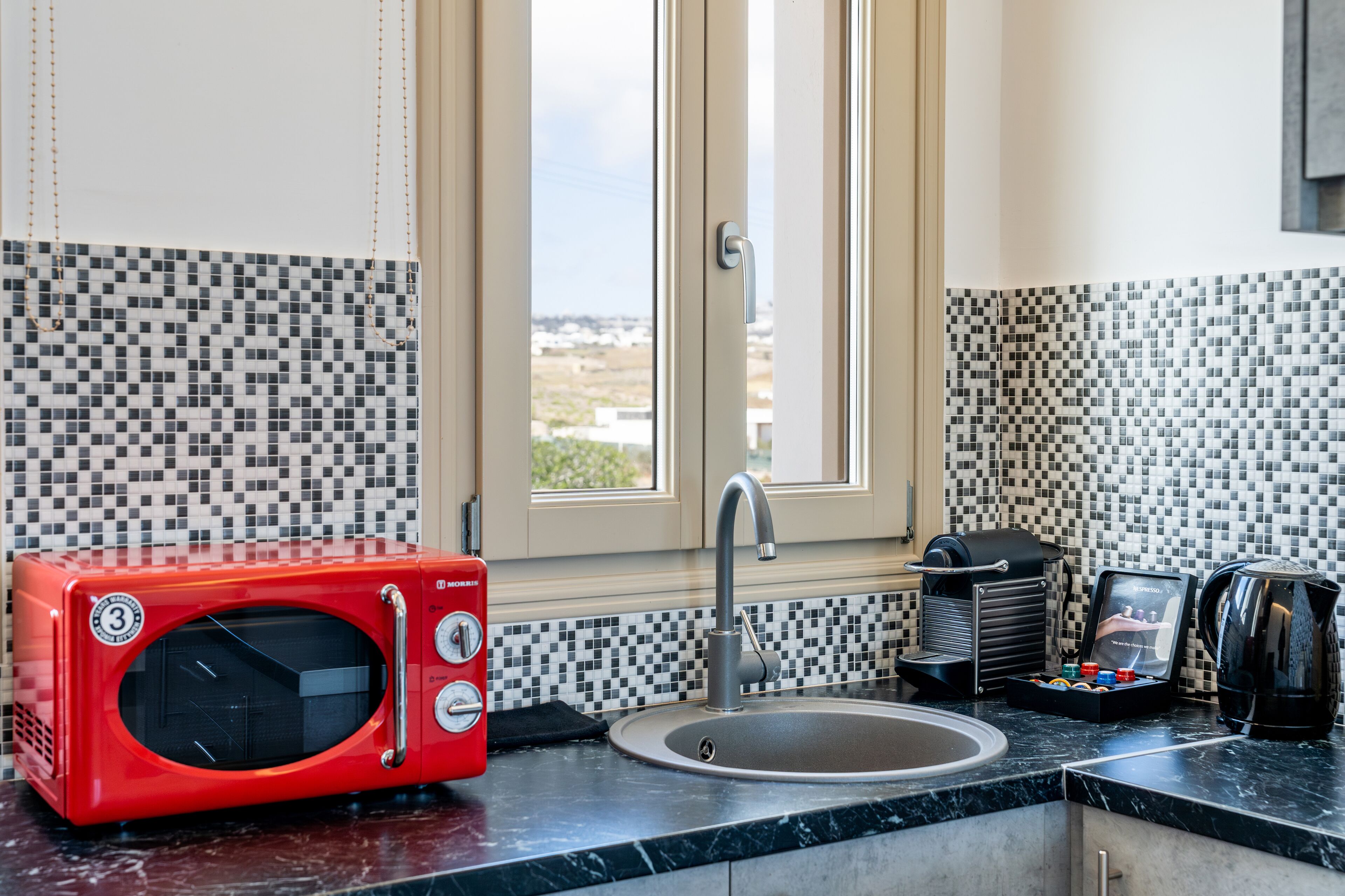 A kitchen with a red microwave, a sink, and a window with a view.