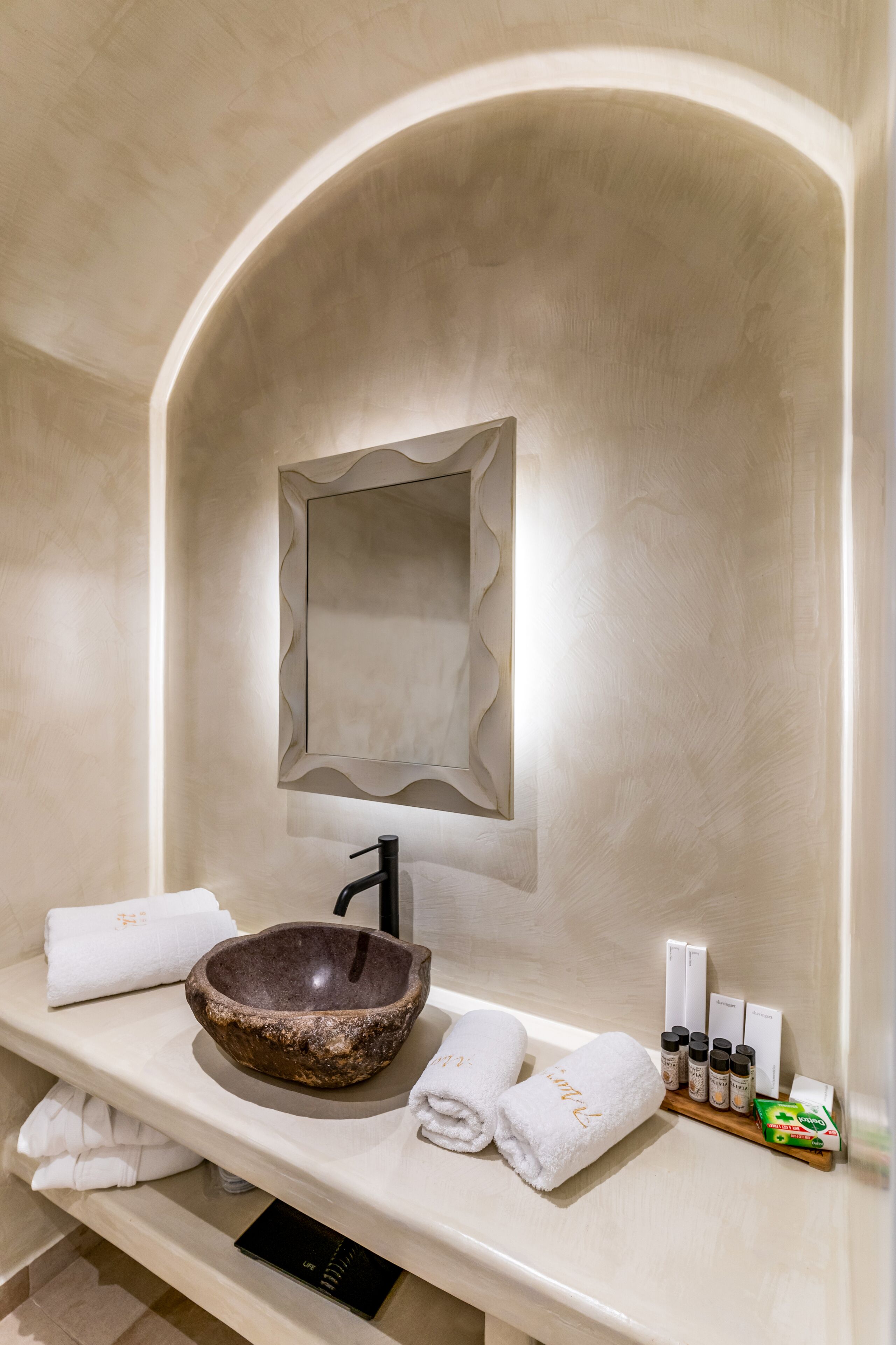 Un baño moderno con un lavabo de piedra color beige, un espejo grande y artículos de tocador ordenados.