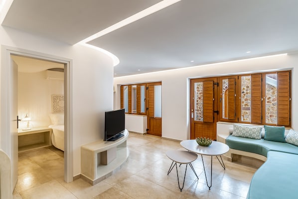 A modern living room with a flat-screen TV, a small round table, and a sofa with patterned cushions. - Marvarit Suites (Santorini)
