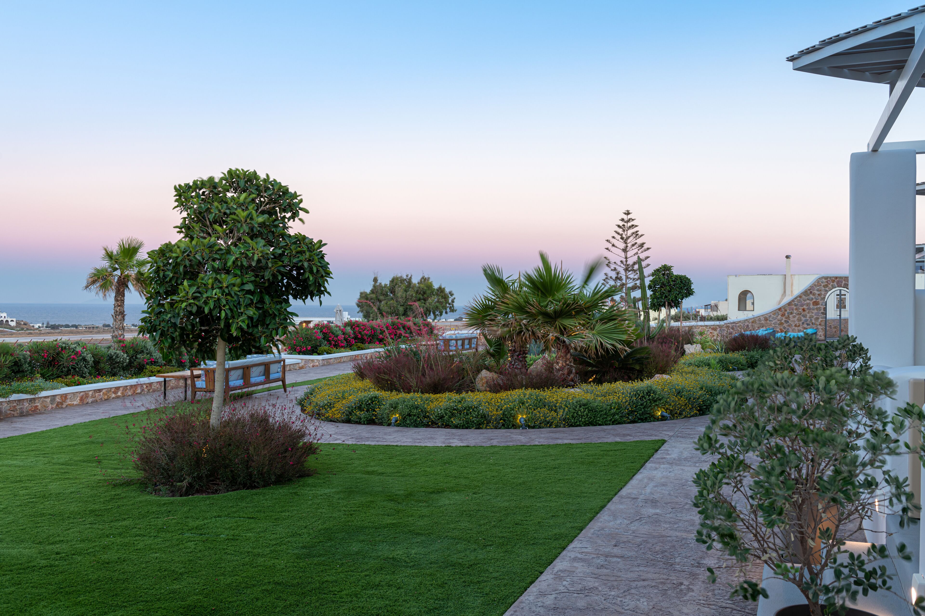 Un jardín ajardinado con un sendero, palmeras y vistas al océano.