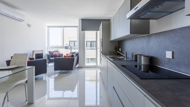 A modern kitchen with a sleek design, a glass dining table, and a view to the living area. - San Giljan Stylish Apartment (St. Julian's)