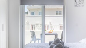 A hotel room with a bed, a set of towels, a small table with fruit and juice, and a balcony with a view of buildings. - San Giljan Stylish Apartment (St. Julian's)