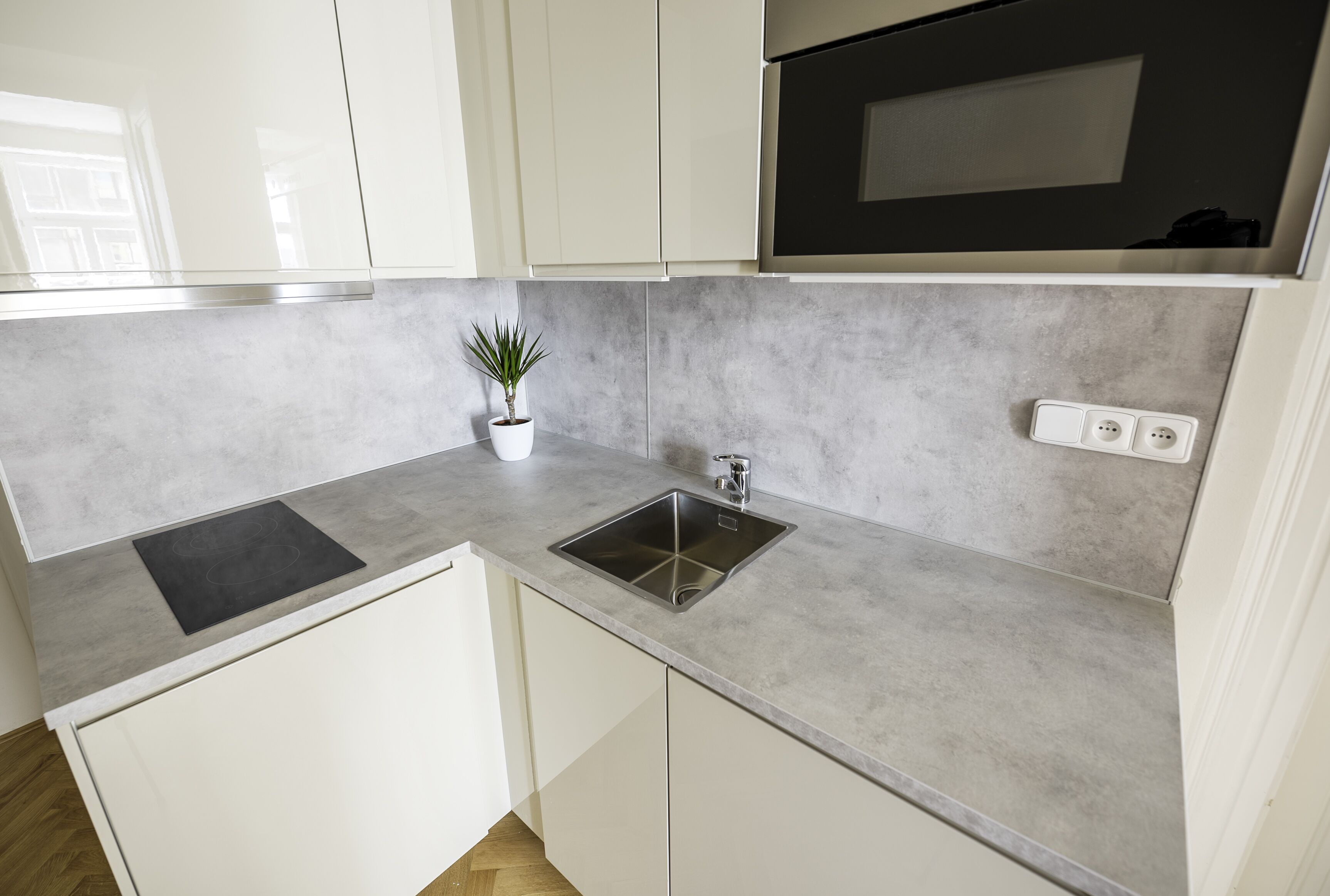 A kitchen with white cabinets, a grey countertop, a black microwave, and a small potted plant.
