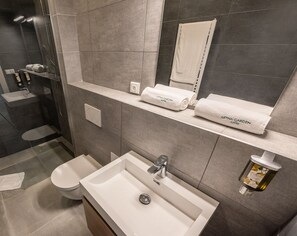 A modern bathroom with a large sink, toilet, and shower area. There are two towel dispensers and a bottle of hand soap on the counter. - Letna Garden Suites (Prague)
