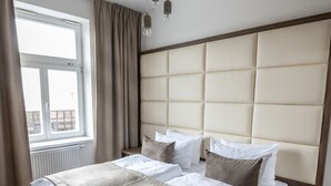 A hotel room with a large bed, a window with curtains, a wooden floor, and a headboard with a padded design. - Letna Garden Suites (Prague)
