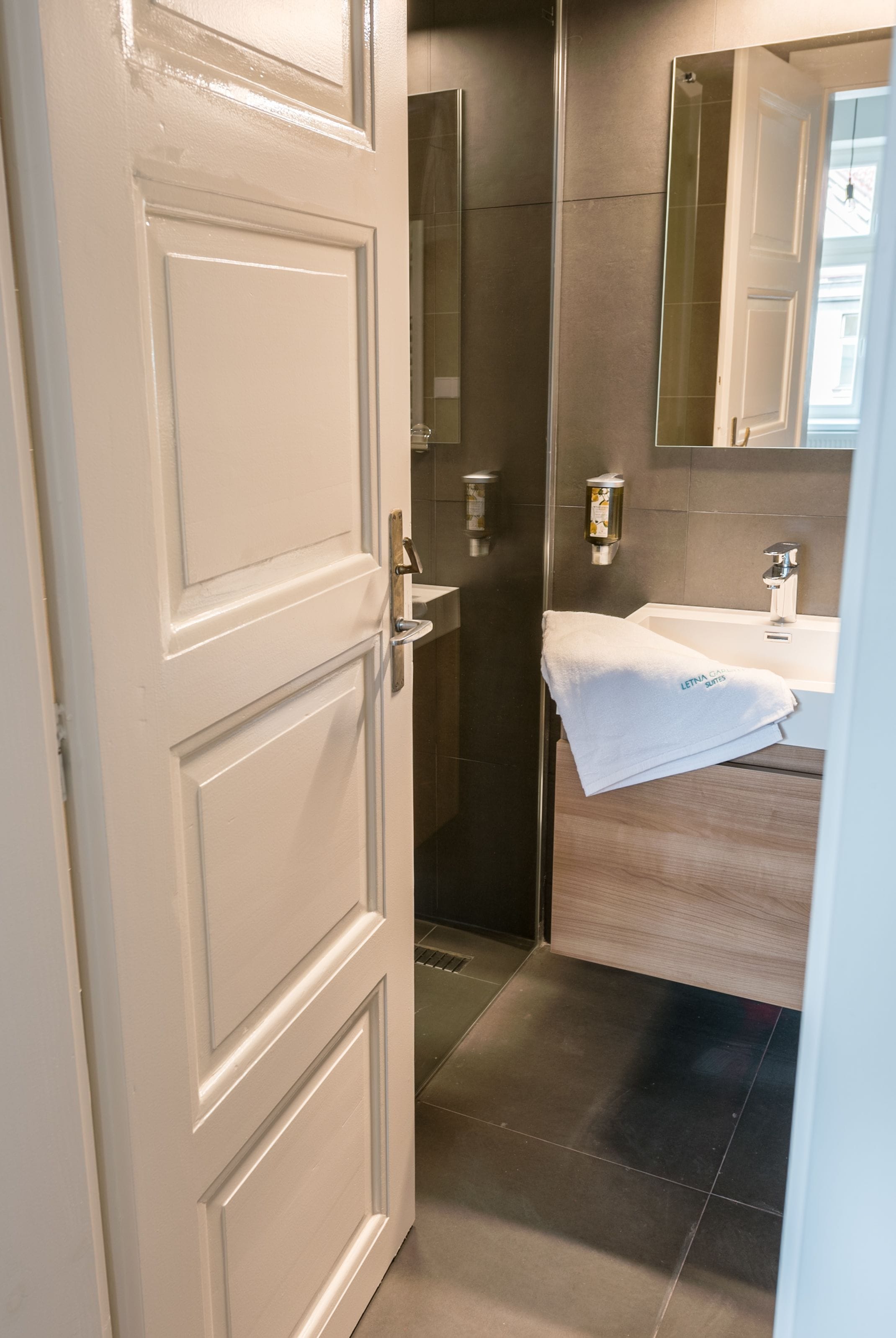 A modern bathroom with a white door, a glass shower enclosure, and a sink with a towel hanging on the wall.