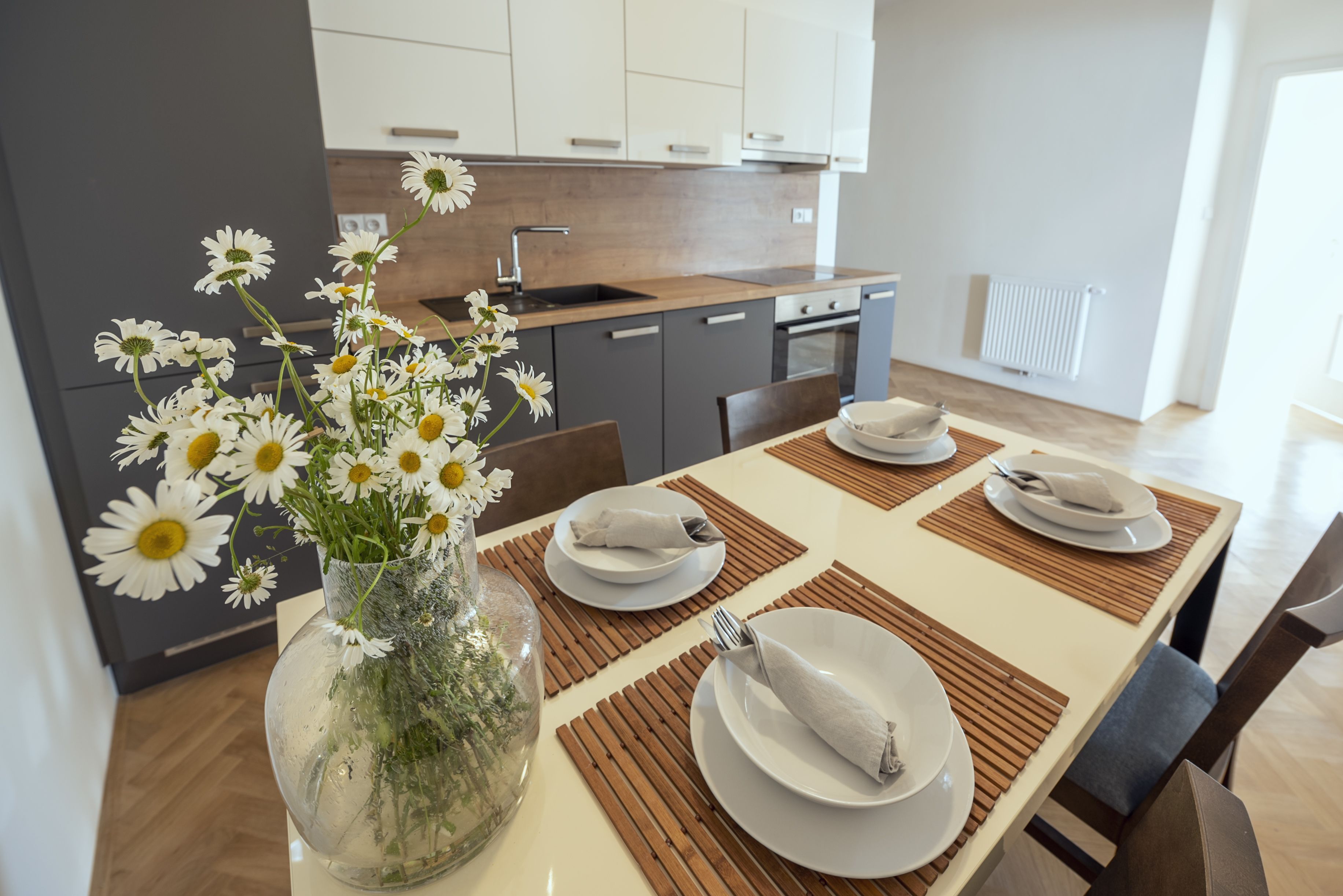 Una cocina moderna con armarios blancos, encimera de madera y un comedor con platos blancos y un florero con margaritas.