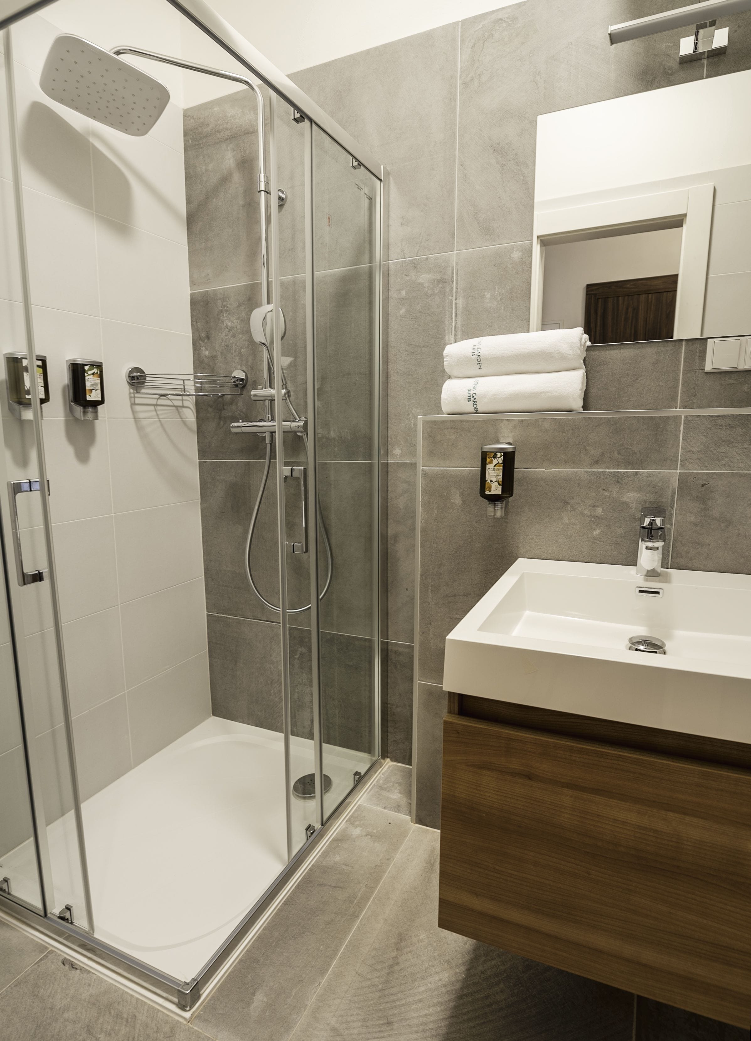 A modern bathroom with a glass-enclosed shower, a white sink, and a wooden vanity.