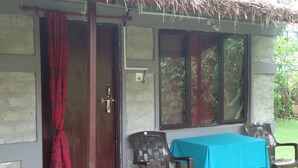 A small room with a table and two chairs, a red curtain, and a window with a view of greenery. - Gurkha Lodge (Pokhara)