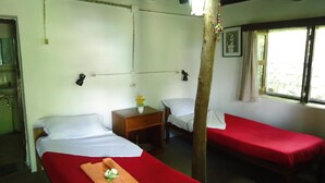 A room with two single beds, a small wooden nightstand with a vase of flowers, a wall-mounted lamp, and a window with curtains. - Gurkha Lodge (Pokhara)