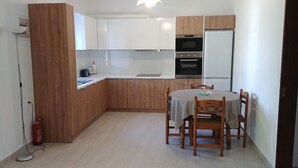 A compact kitchen with wooden cabinets, a built-in oven, and a dining table with chairs. - Dora Apartments (Zakynthos)