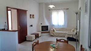A living room with a fireplace, sofa, dining table, and a small side table. - Dora Apartments (Zakynthos)